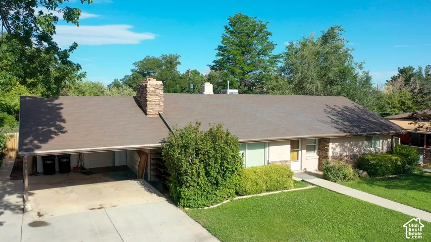 Ranch-style residence featuring a stone chimney, covered carport, and a manicured front lawn
