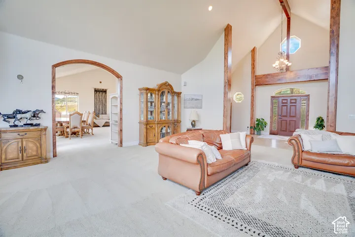 Vaulted ceilings with exposed wood beams, arched entryway, double front entry doors with sidelights, and a decorative chandelier