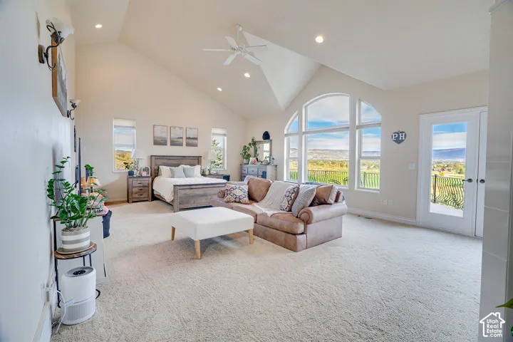 Vaulted ceiling with recessed lighting and ceiling fan, large arched windows, french doors with balcony access, and light neutral carpeting