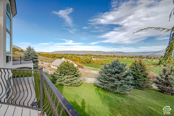 Balcony with decorative metal railing, expansive green lawn, mature evergreen trees, distant hills, and rural landscape