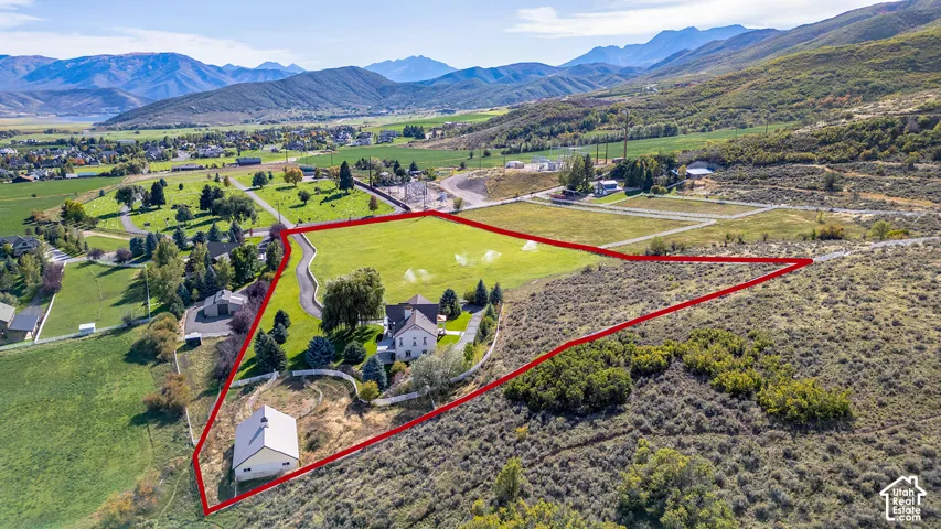 Expansive property featuring a main residence, a secondary detached structure, a paved driveway, and established landscaping, all set against a backdrop of distant mountains