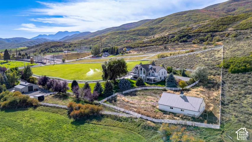 Expansive property featuring a two-story residence, separate outbuilding, manicured grounds, white fencing, and natural mountain scenery