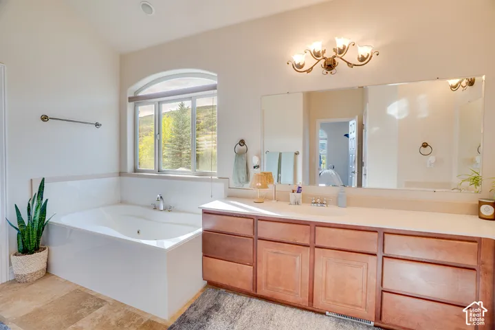 Built-in soaking tub with arched window, dual vanity with wood cabinetry, and large wall-mounted mirror