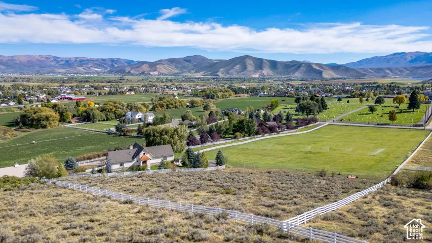 Expansive green spaces with distant mountain backdrop, featuring a white fence, scattered trees, and residential structures
