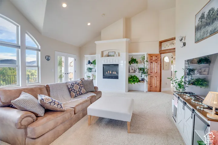 Vaulted ceiling with recessed lighting, fireplace with mantel, built-in shelving, glass-paned French doors, and large windows