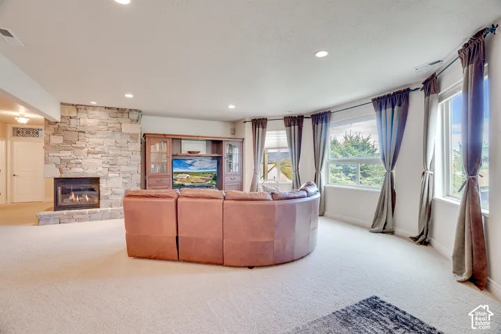 Curved room design with multiple windows, recessed lighting, stone-clad fireplace with hearth, and light-toned carpet flooring