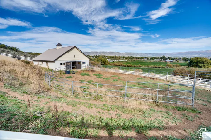 Barn structure with cupola and weathervane, metal fencing, white perimeter fence, and expansive natural landscape