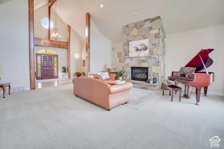 Vaulted ceilings with exposed beams, stone fireplace, light-colored carpeting, recessed lighting, and a wood entry door with sidelights