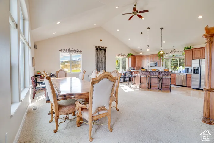 Vaulted ceiling with recessed lighting, large windows, wood-finish cabinetry, stainless steel appliances, and a kitchen island with pendant lighting