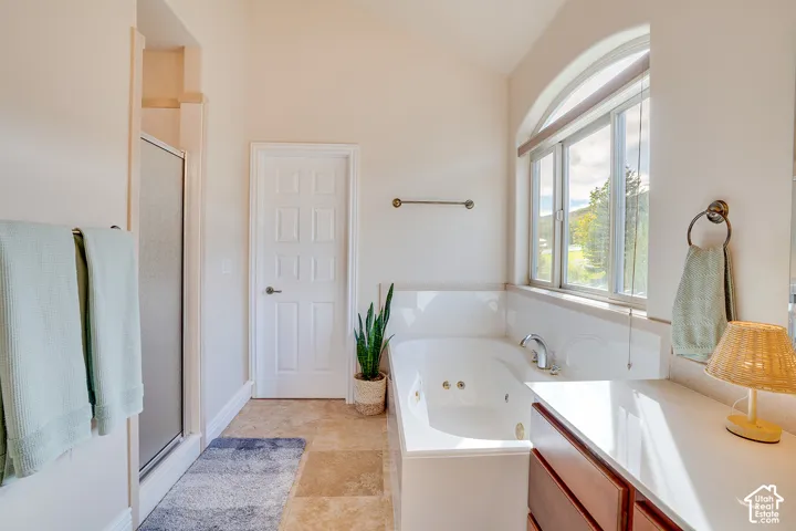 Tiled flooring with a built-in jetted tub, a window with an arched transom, a glass-enclosed shower, and a vanity with a white countertop