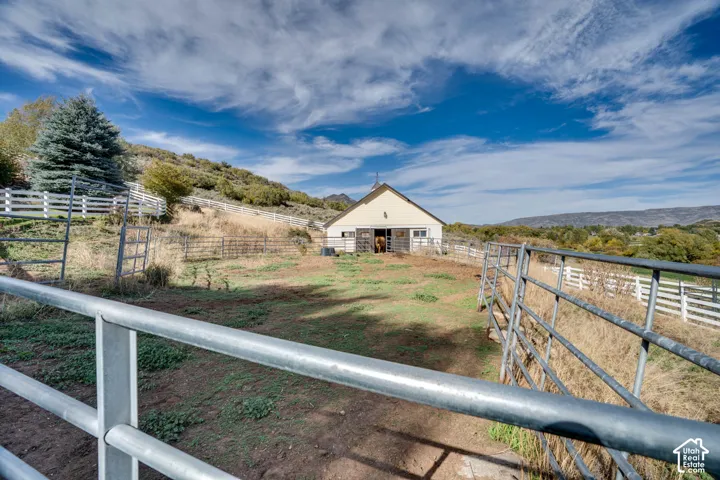 Barn structure with white siding and a brown roof, featuring metal paddock fencing