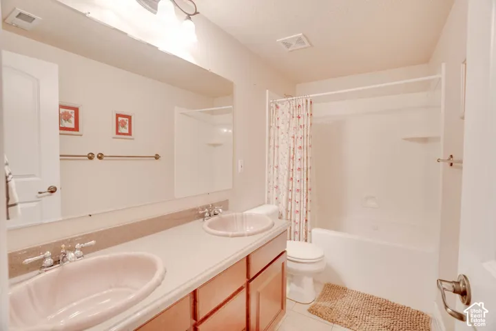 Dual basin vanity with a light-colored countertop, wood-finish cabinetry, and an integrated bathtub/shower combination