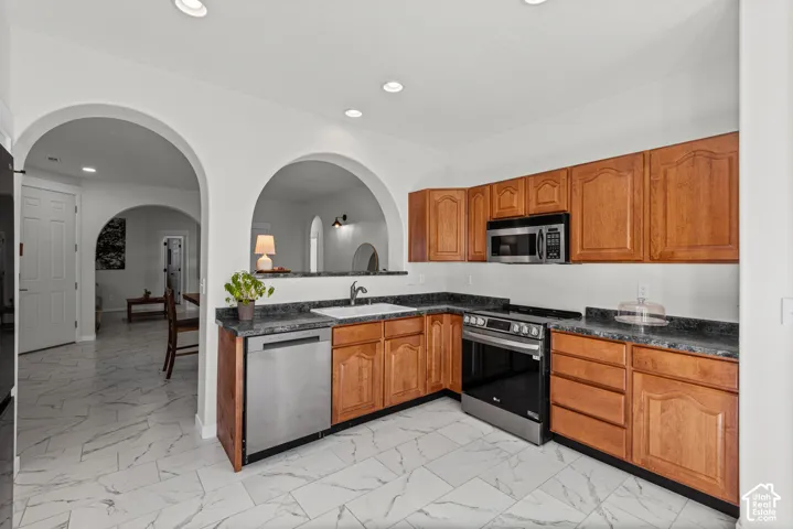 Kitchen featuring wood cabinetry, stainless steel appliances, dark countertops, and white tile flooring
