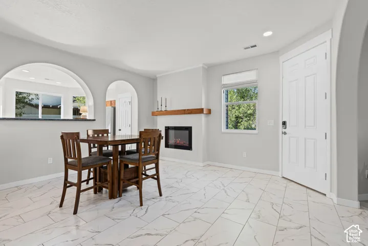 White-toned tile flooring, integrated electric fireplace with wood mantel, arched wall openings, and a white paneled door