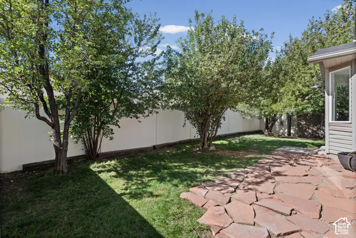 Lawn area with mature trees, a privacy fence, and a stone patio