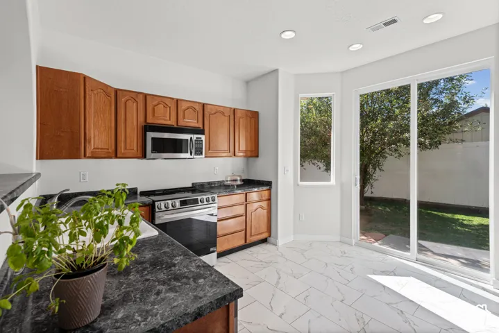 Kitchen featuring wood cabinetry, stainless steel appliances, dark countertops, and white tile flooring
