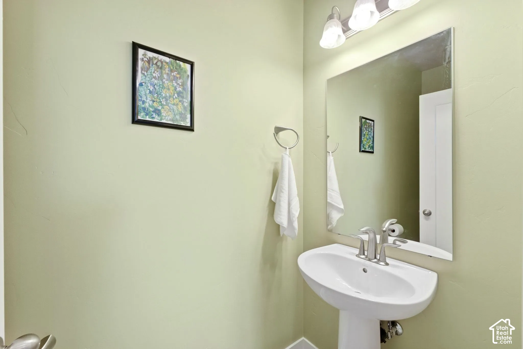 Pedestal sink with a brushed nickel faucet, large wall mirror, and a three-light vanity fixture