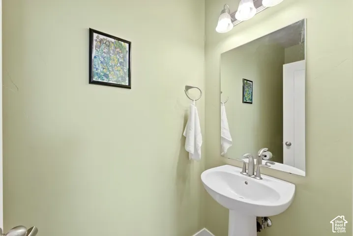 Pedestal sink with a brushed nickel faucet, large wall mirror, and a three-light vanity fixture