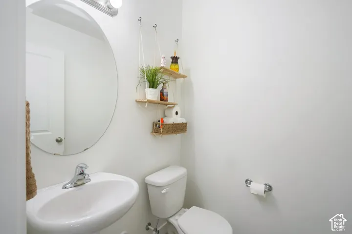 Pedestal sink with a chrome faucet, round wall-mounted mirror, and a two-piece toilet