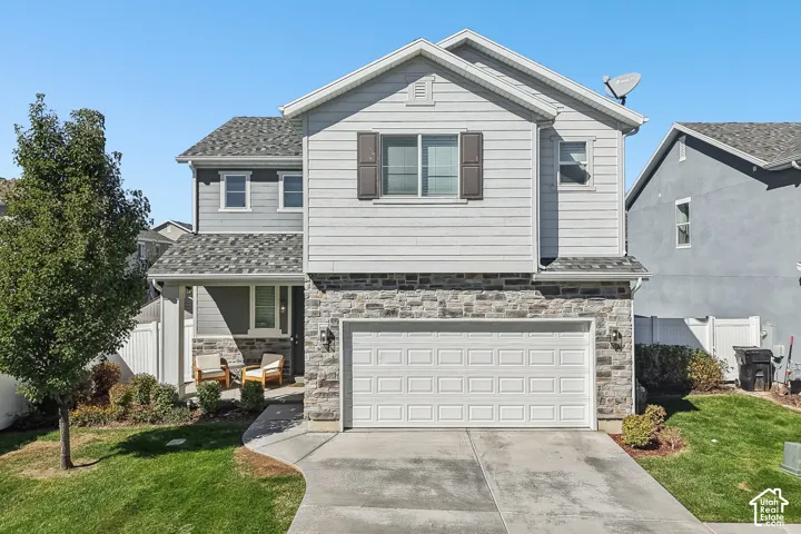 Two-story residence featuring a stone and siding exterior, an attached garage, a covered front porch, and a concrete driveway