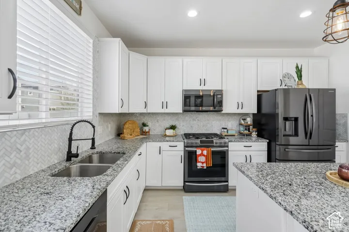 White cabinetry with black hardware, stone-finish countertops, stainless steel appliances, herringbone tile backsplash, and a double basin sink with a gooseneck faucet