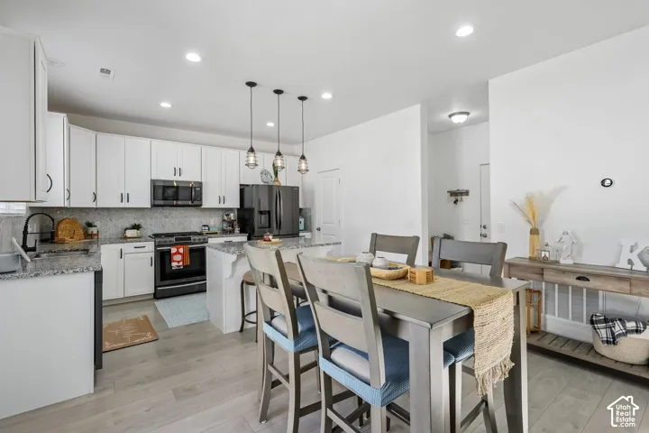 Kitchen featuring white cabinetry, a large kitchen island with pendant lighting, black appliances, a tile backsplash, and light wood-finish flooring
