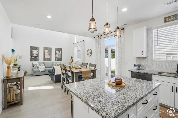 Kitchen island with granite countertop, white cabinetry with dark pulls, herringbone tile backsplash, and three pendant lights