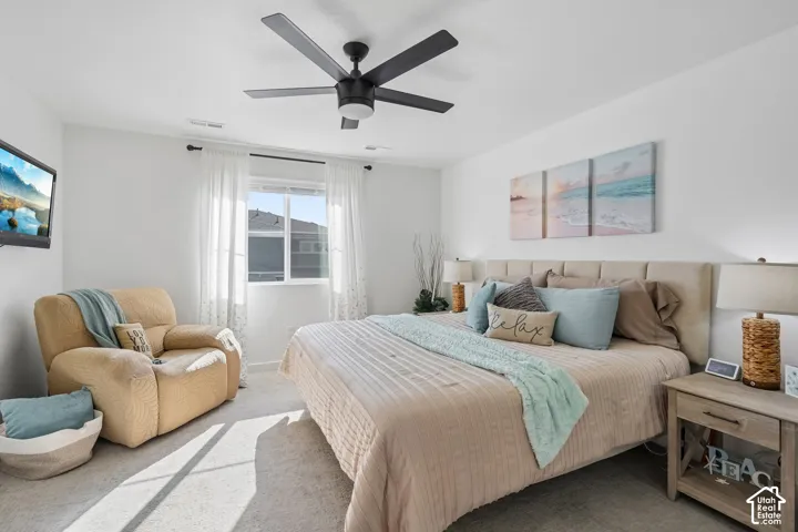 Recessed lighting, ceiling fan with light fixture, window with sheer curtains, upholstered headboard, and wood-finish nightstands