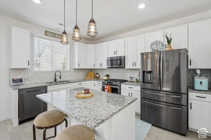 White cabinetry with black hardware, granite countertops, stainless steel appliances, a kitchen island with seating, and wood-finish flooring