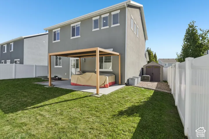 Grassed backyard featuring a concrete patio with a modern pergola, a storage shed, and white vinyl perimeter fencing