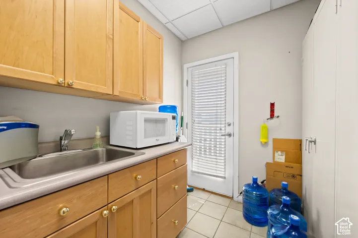 Light wood cabinetry, stainless steel sink, tile flooring, and a solid exterior door with blinds