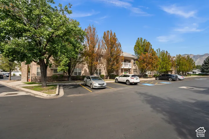 Paved parking lot with marked spaces, bordered by a multi-story building featuring balconies, and mature trees