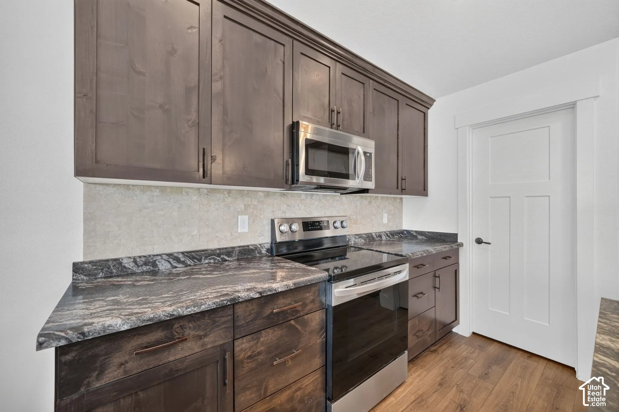 Dark wood-finish cabinetry with crown molding, stainless steel microwave, black electric range, patterned countertops, and wood-finish flooring