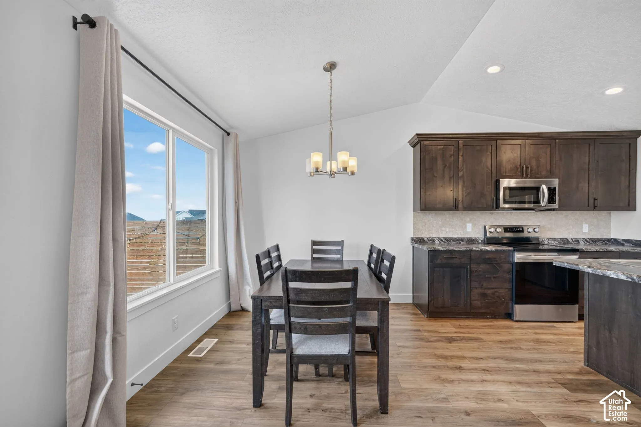 Vaulted ceilings, wood-finish flooring, stainless steel appliances, dark wood cabinetry, and a stone-look countertop