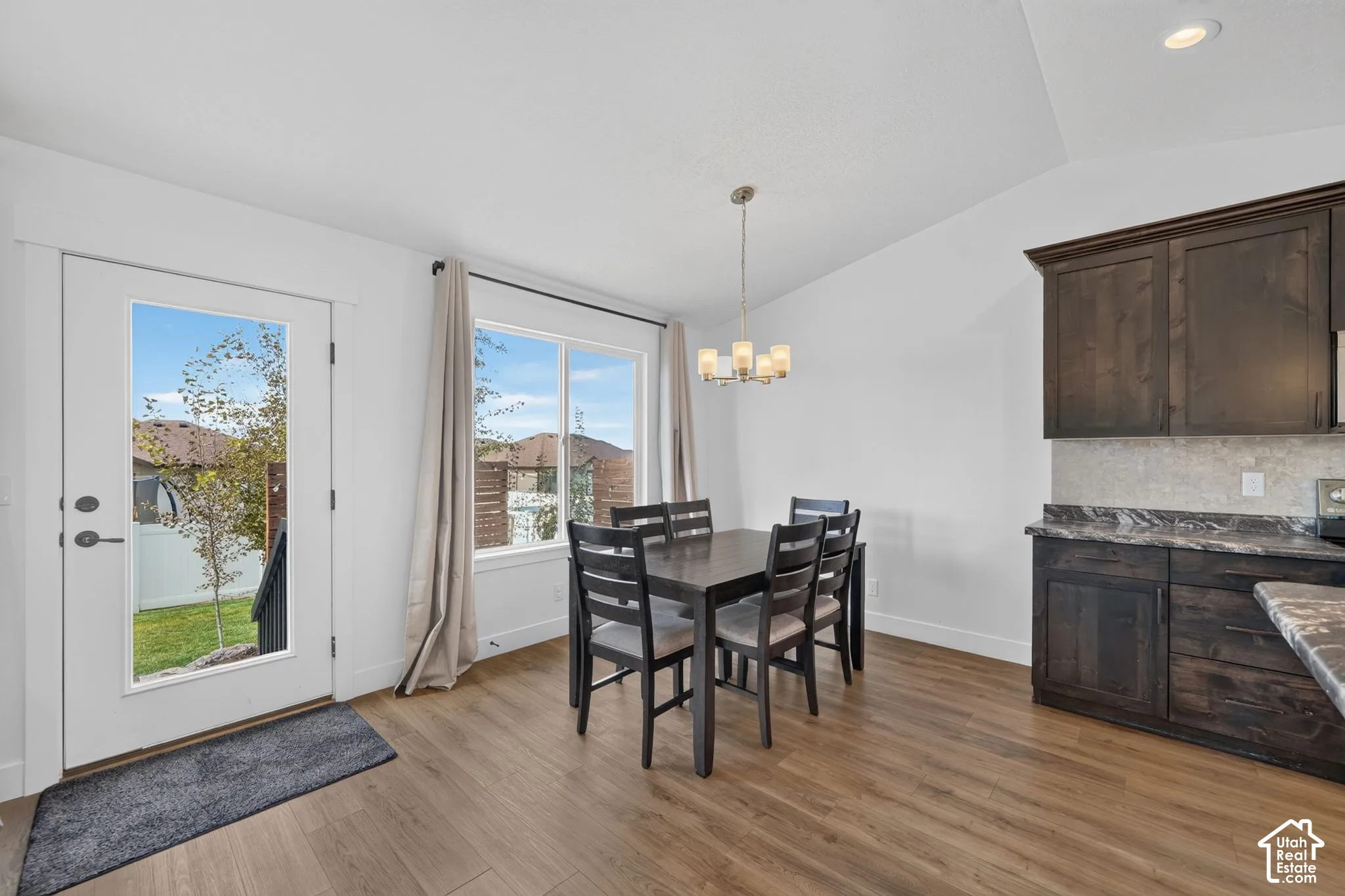 Wood-finish flooring, vaulted ceiling, built-in dark wood cabinetry, window with backyard views, and glass-paned exterior door