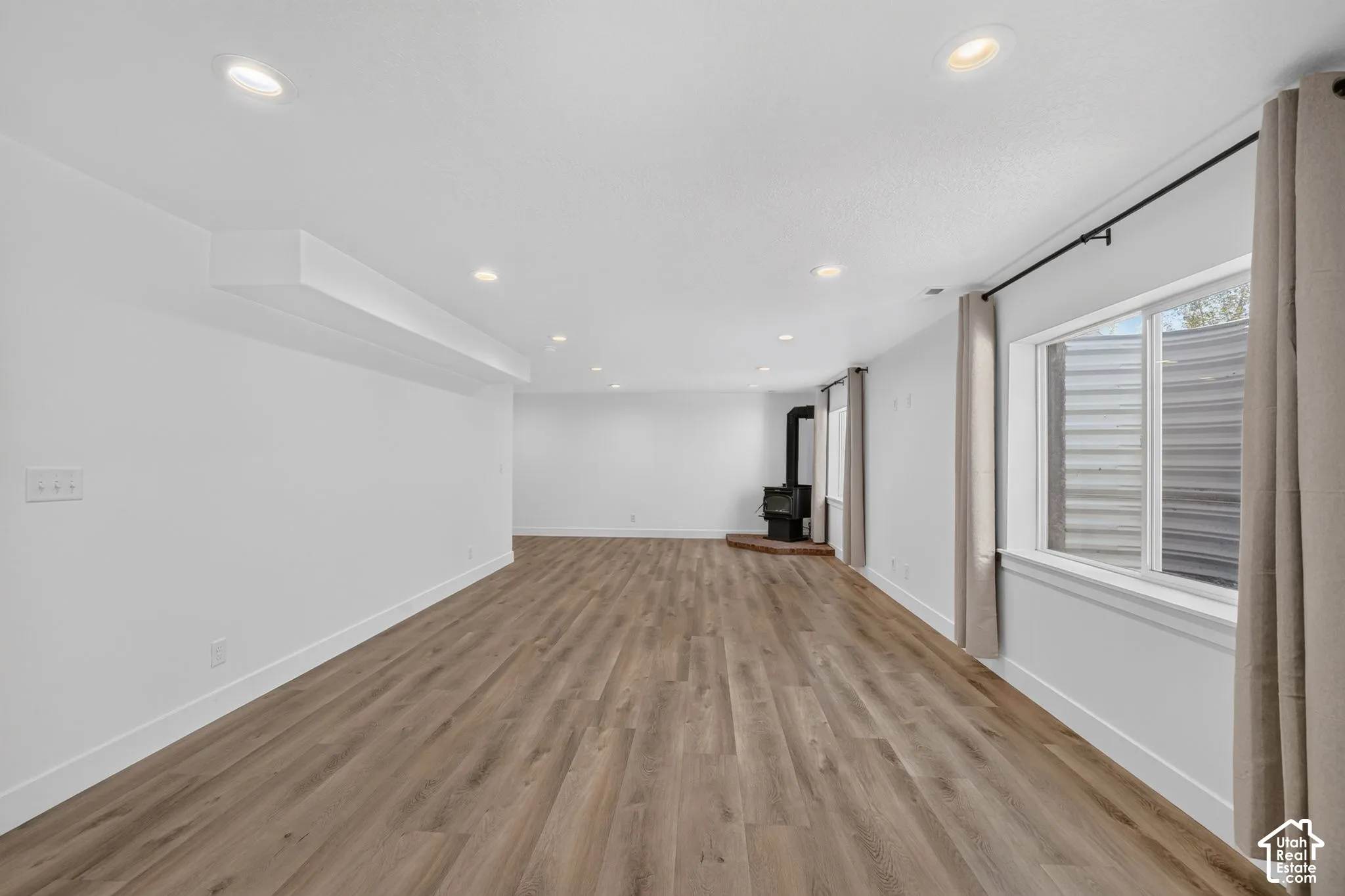Spacious room featuring wood-finish flooring, recessed lighting, and a freestanding fireplace with a brick hearth