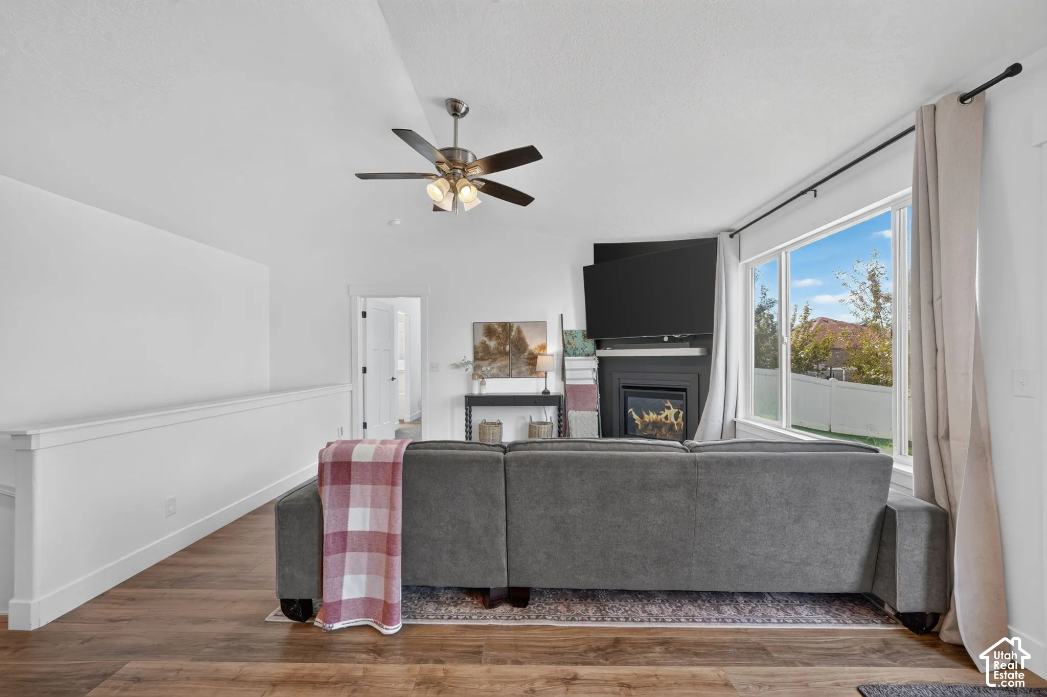 Living area featuring wood-finish flooring, a contemporary fireplace with a dark mantel, large windows, a ceiling fan, and a white interior railing