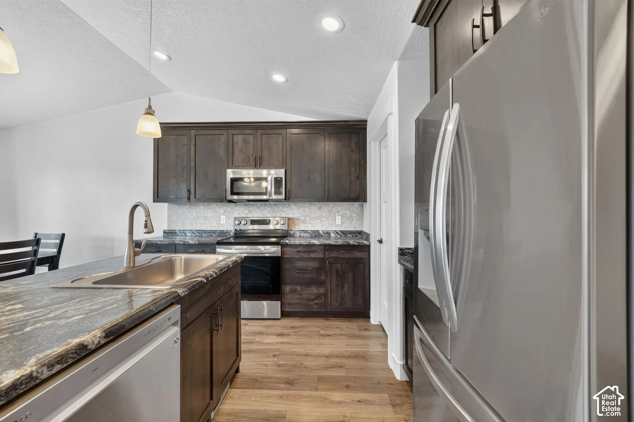 Kitchen featuring dark wood-finish cabinetry, stainless steel appliances, speckled countertops, and wood-finish flooring