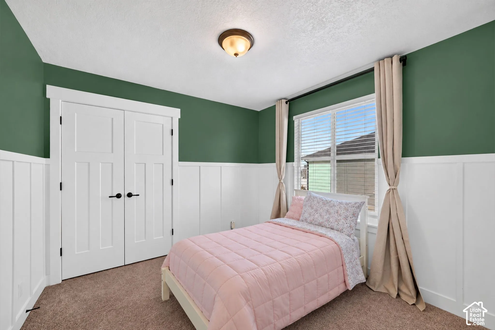 Board and batten wall paneling, large window with blinds, ceiling-mounted light fixture, and textured carpeting