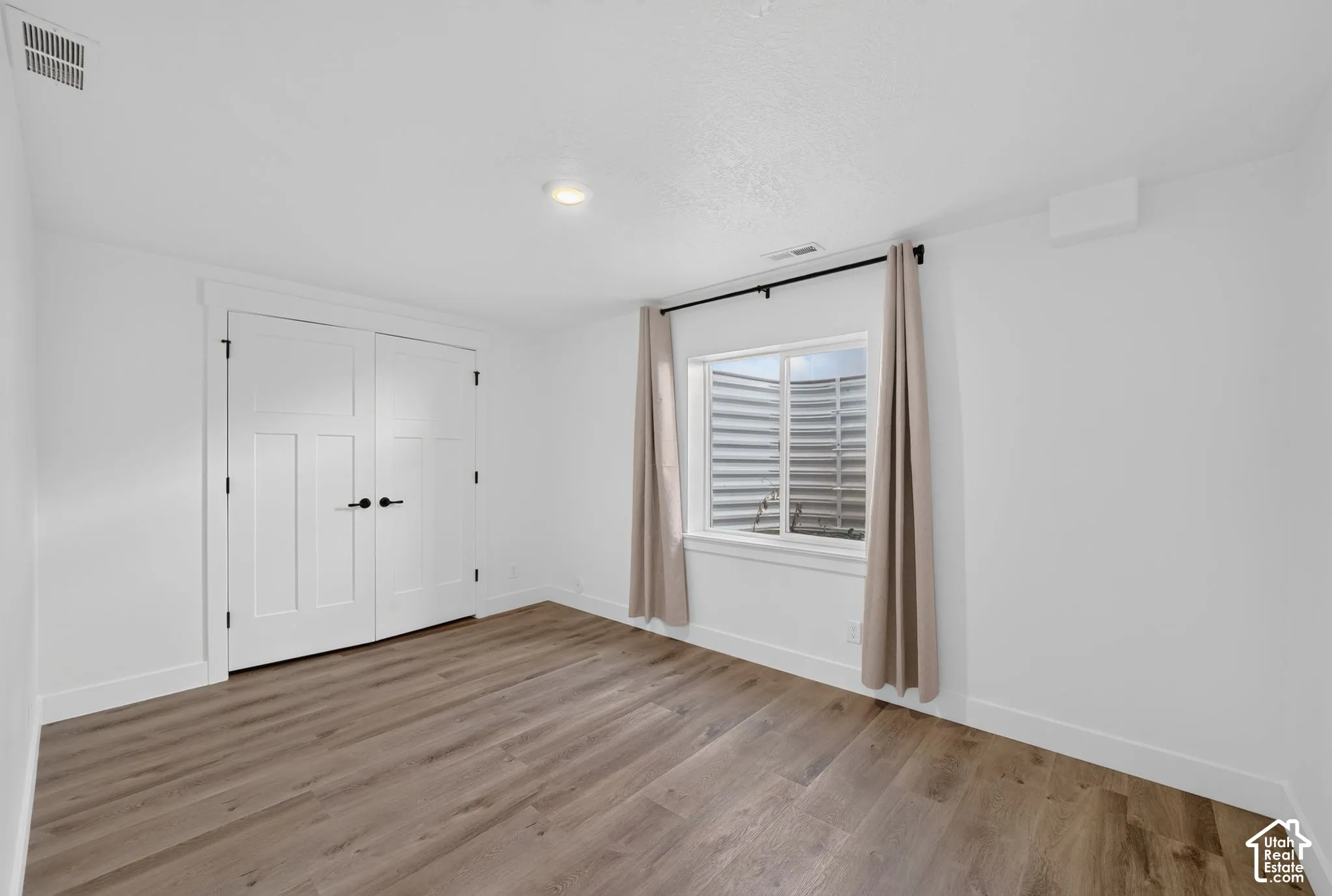 Wood-finish flooring, recessed lighting, white walls, and a window with a window well