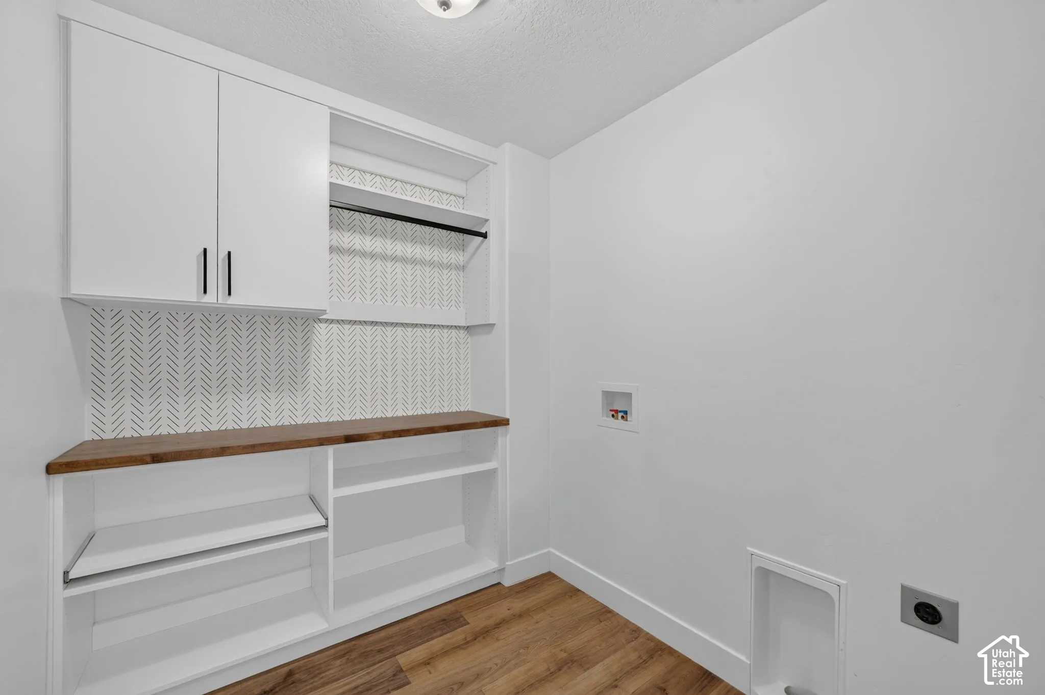 White cabinetry with matte black hardware, wood-finish countertop, patterned accent wall, and built-in shelving