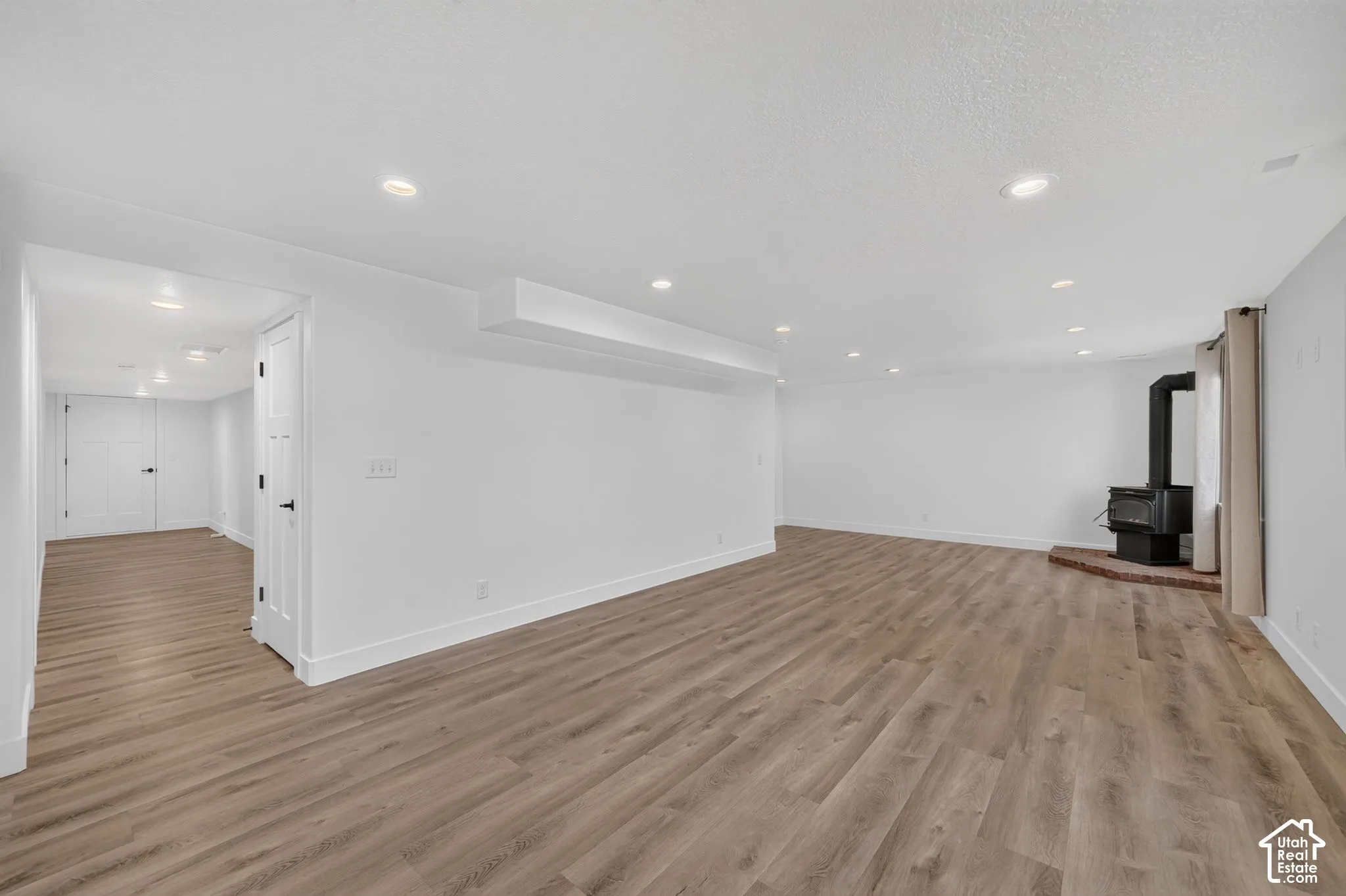 Spacious room featuring wood-finish flooring, recessed lighting, and a black wood-burning stove on a brick hearth