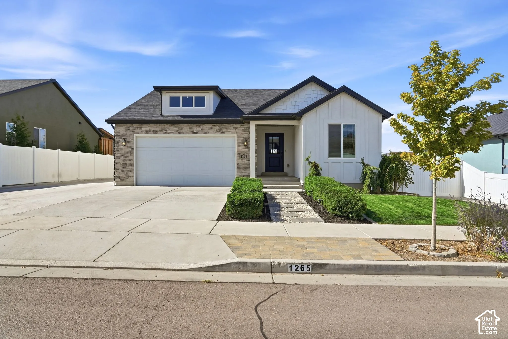 Contemporary exterior with a stone and vertical siding facade, dormer window, two-car garage, and concrete driveway