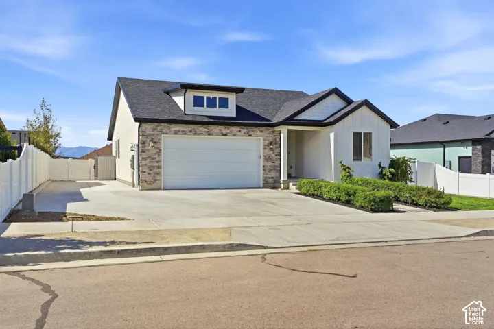 Contemporary exterior featuring a stone and siding facade, an attached two-car garage, a concrete driveway, and a white vinyl fence