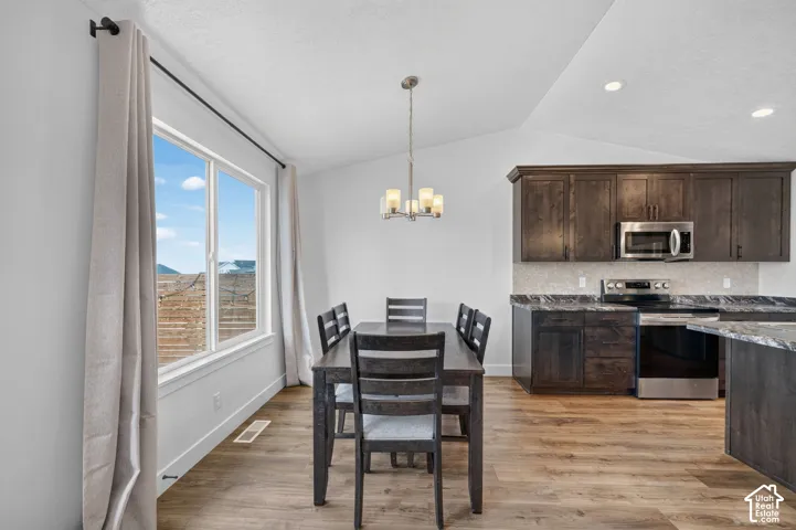 Vaulted ceilings, wood-finish flooring, stainless steel appliances, dark wood cabinetry, and a stone-look countertop