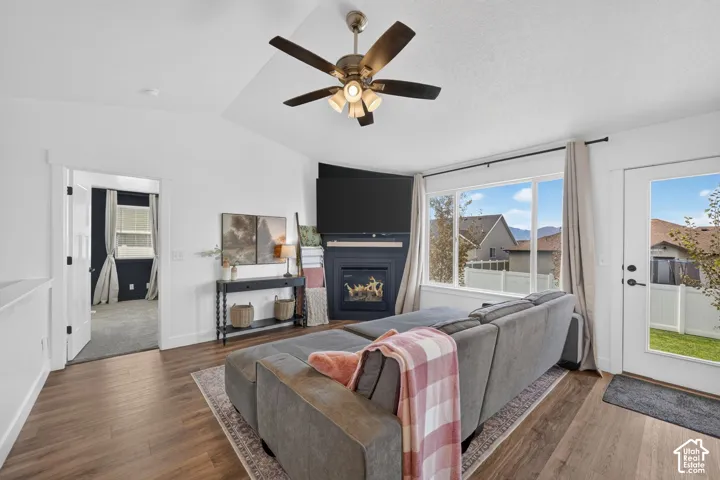 Living area featuring wood-finish flooring, an angled fireplace with built-in media space, large windows, a ceiling fan, and a glass-paneled exterior door