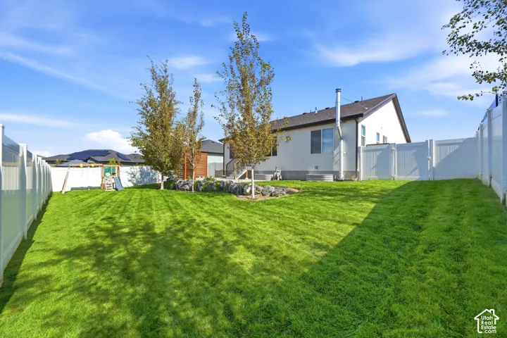 Expansive backyard featuring a manicured lawn, established trees, and white privacy fencing