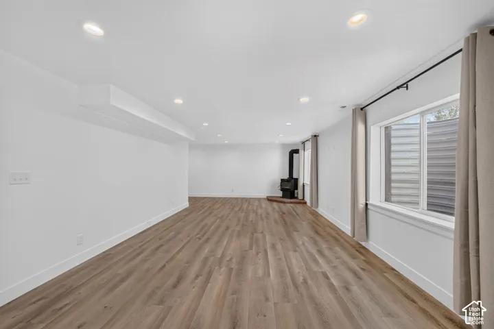 Spacious room featuring wood-finish flooring, recessed lighting, and a freestanding fireplace with a brick hearth