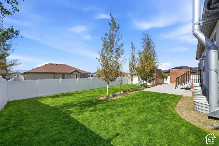 Expansive backyard featuring a manicured lawn, established trees, concrete patio, and privacy fencing