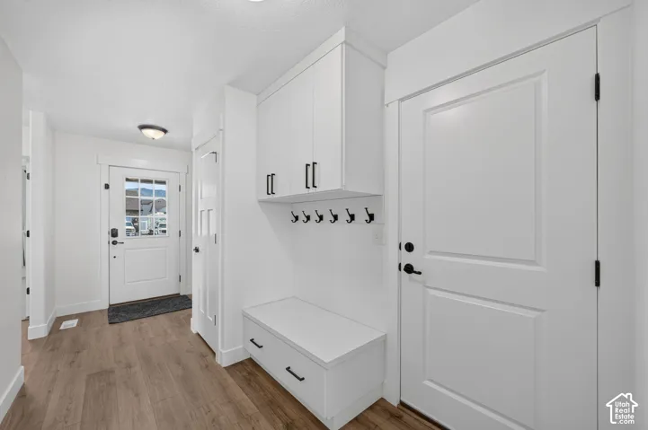Entryway featuring wood-finish flooring, a white paneled door with glass inserts, built-in storage bench with drawers, white upper cabinetry, and matte black hardware